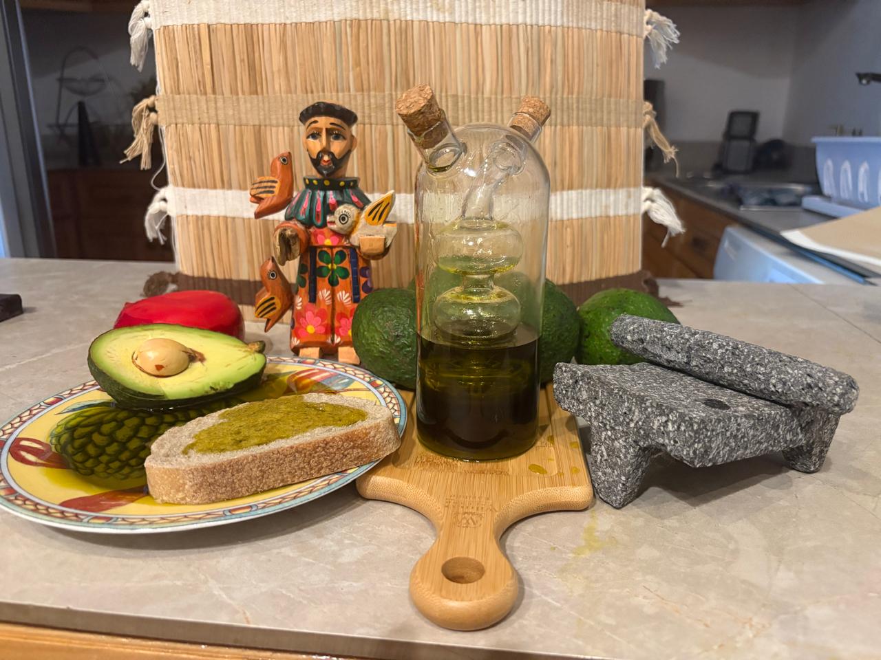 Artisanal avocado oil from Guatemala with fresh bread, avocado, and traditional stone grinder.